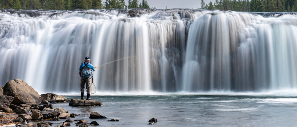 An angler fishing in front of a gorgeous waterfall
